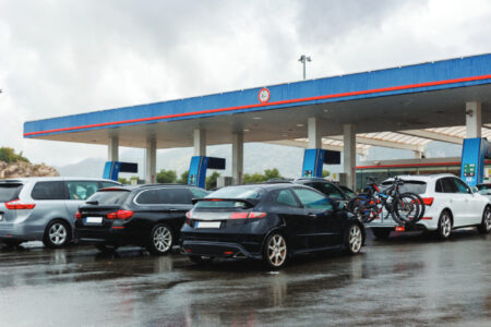 Multiple cars queue waiting refuel at gas station overcast cloudy sky background n rainy day.…